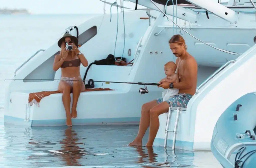 Sailing La Vagabonde - A family is fishing on a catamaran with a baby in the water.