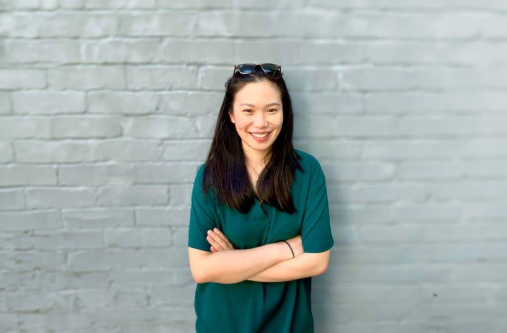 Janice Fung in a green dress standing in front of a brick wall.