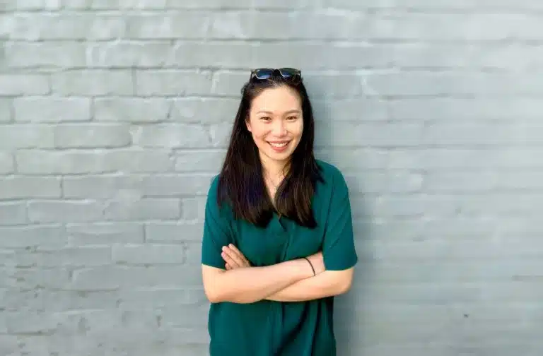 Janice Fung in a green dress standing in front of a brick wall.