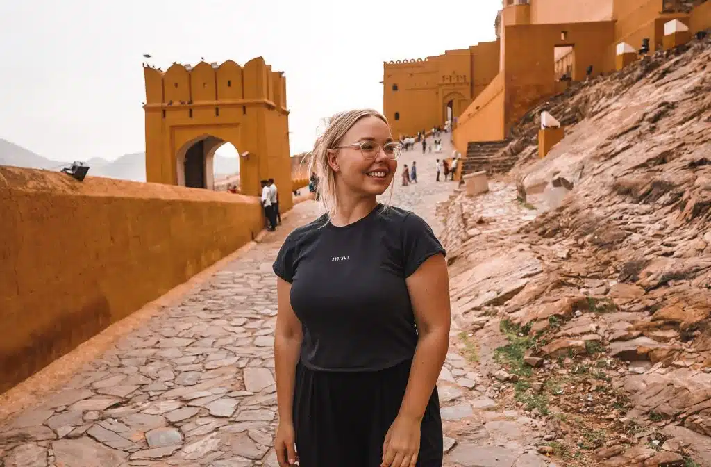 A woman smiling while walking on a stone path next to a yellow fortified wall - josieliftsthings