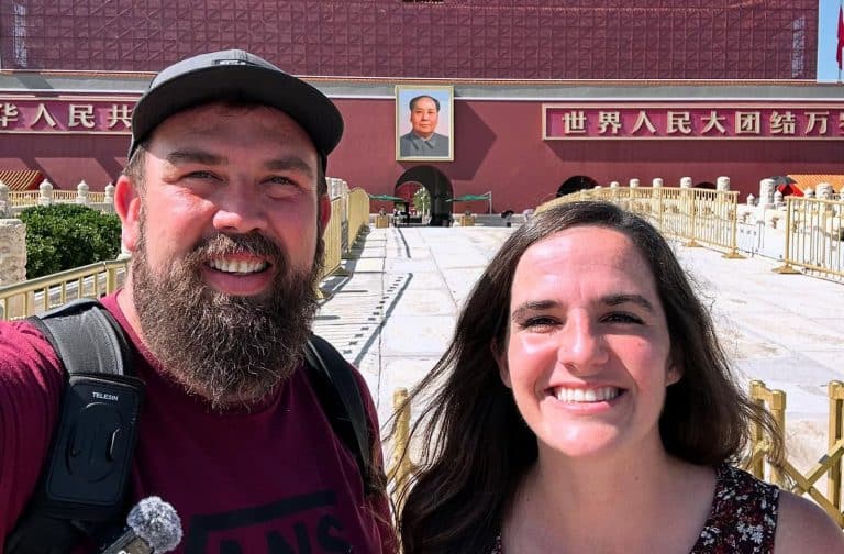 Tim and Ashton stand smiling in front of the entrance to Tiananmen Square in Beijing, with a portrait of Mao Zedong visible in the background—a memorable stop along their Road Less Trekked adventure.
