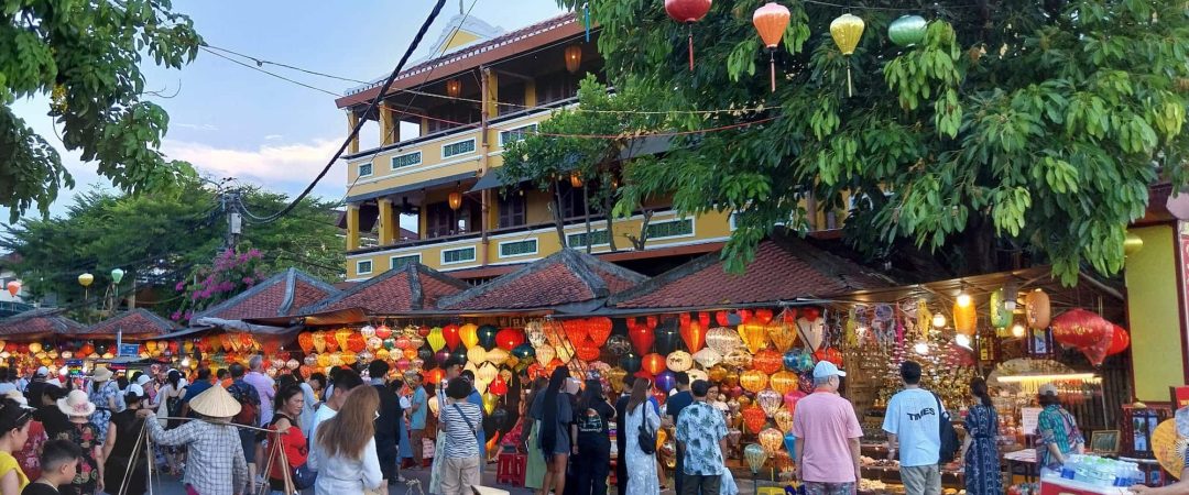 A crowded market with lanterns and people walking around.